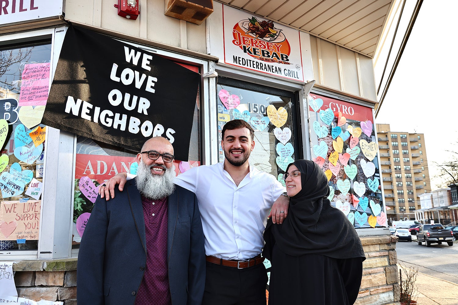 The Emanet Family in front of a sign that says "We Love Our Neighbors"
