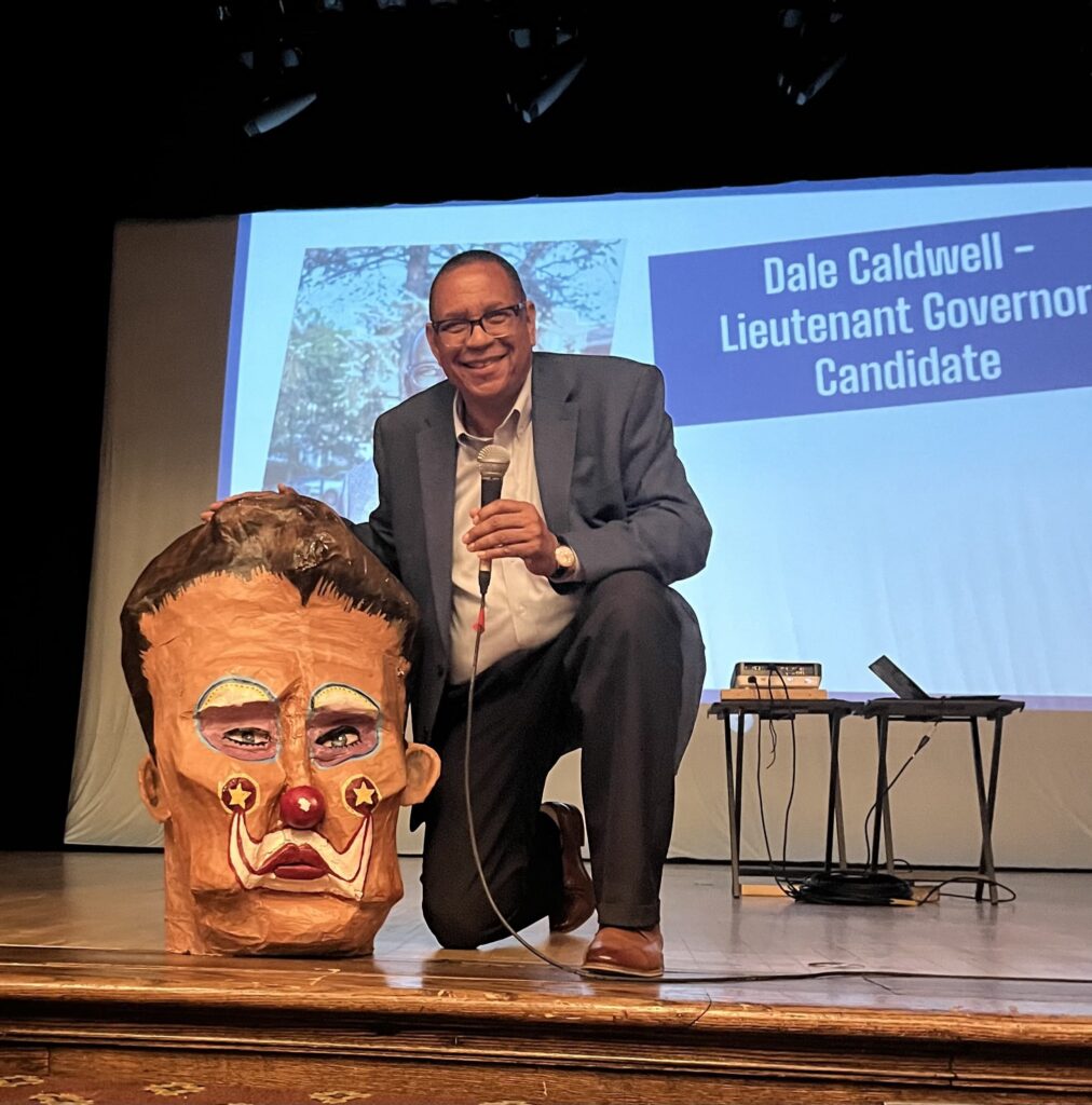 Dale Caldwell Knells in on the stage at the Scottish Rite Auditorium next to the head of one of the caricatures created by the CRI Creative Team
