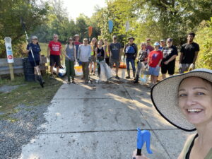 A diverse group of environmental warriors stand on the boat ramp at Newton Lake. There are 15 people lined up with Kayak Paddles, Trash bags, and litter grabbers.