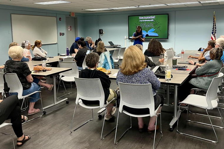 A group of people sit around a table at the Voorhees library watching a teacher bring us tips on learning spanish