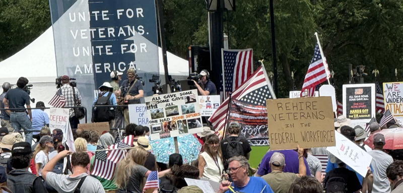 A veteran's protest in DC. WE have a group of people with signs and flags standing in front of a stage
