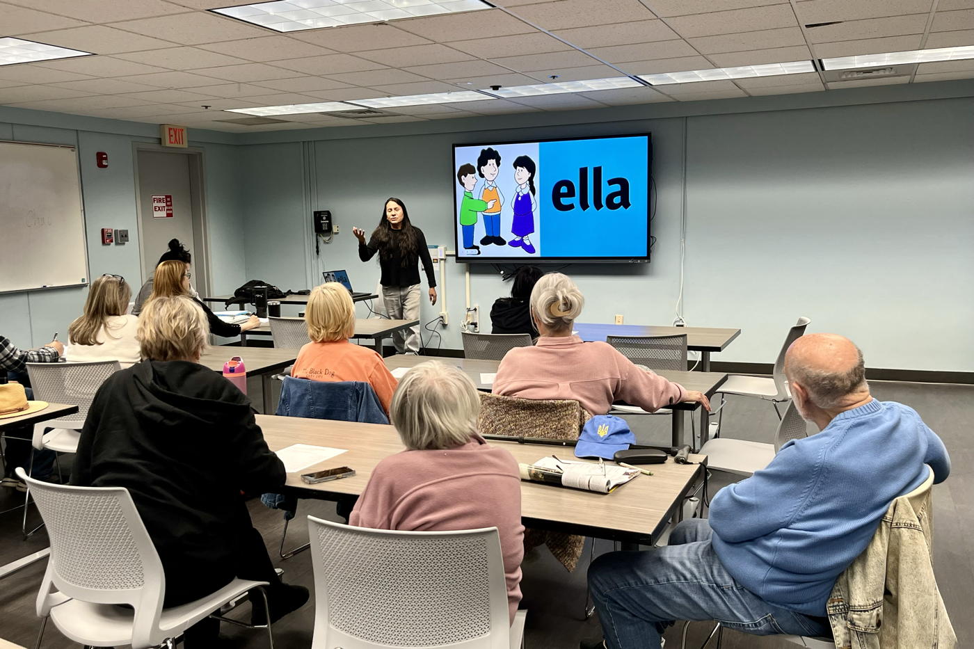 A group of people are learning spanish in the meeting room at Voohees library. A teacher is in the front of the students with a screen behind them. The screen is showing one of the many pronouns in Spanish