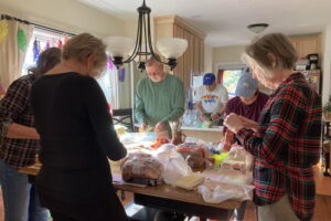 A group of people stand around a kitchen table and make sandwiches for those less fortunate than themselves