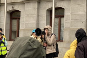 A women stands in front of Philadelphia City Hall speaking into a black Megaphone as people gather around to listen