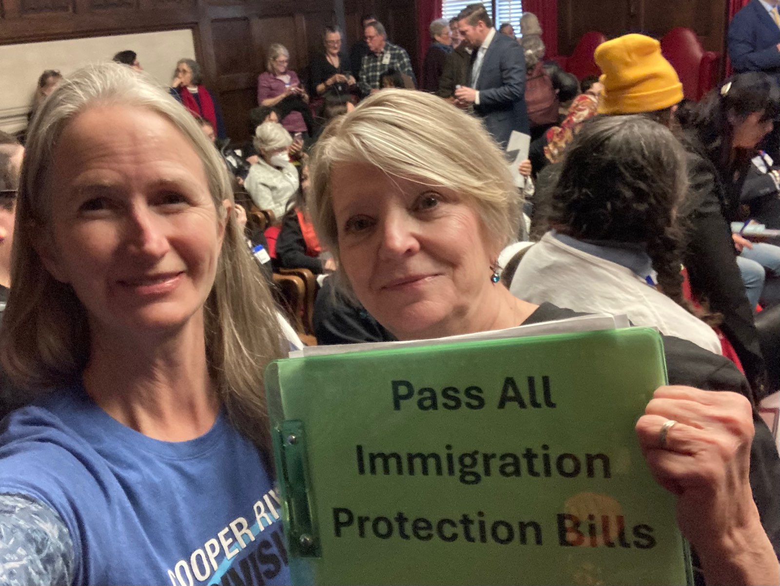 Two CRI members stand with a copy of the bills in front of a very crowded Assembly chamber