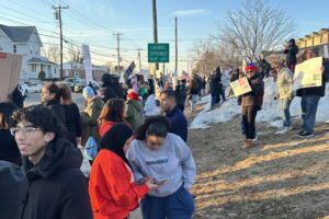 I large group of people gather on the side of the road to protest the presence of ICE in Camden County. A street sign about the crowd reminds Laurel Spring to "Keep Left"