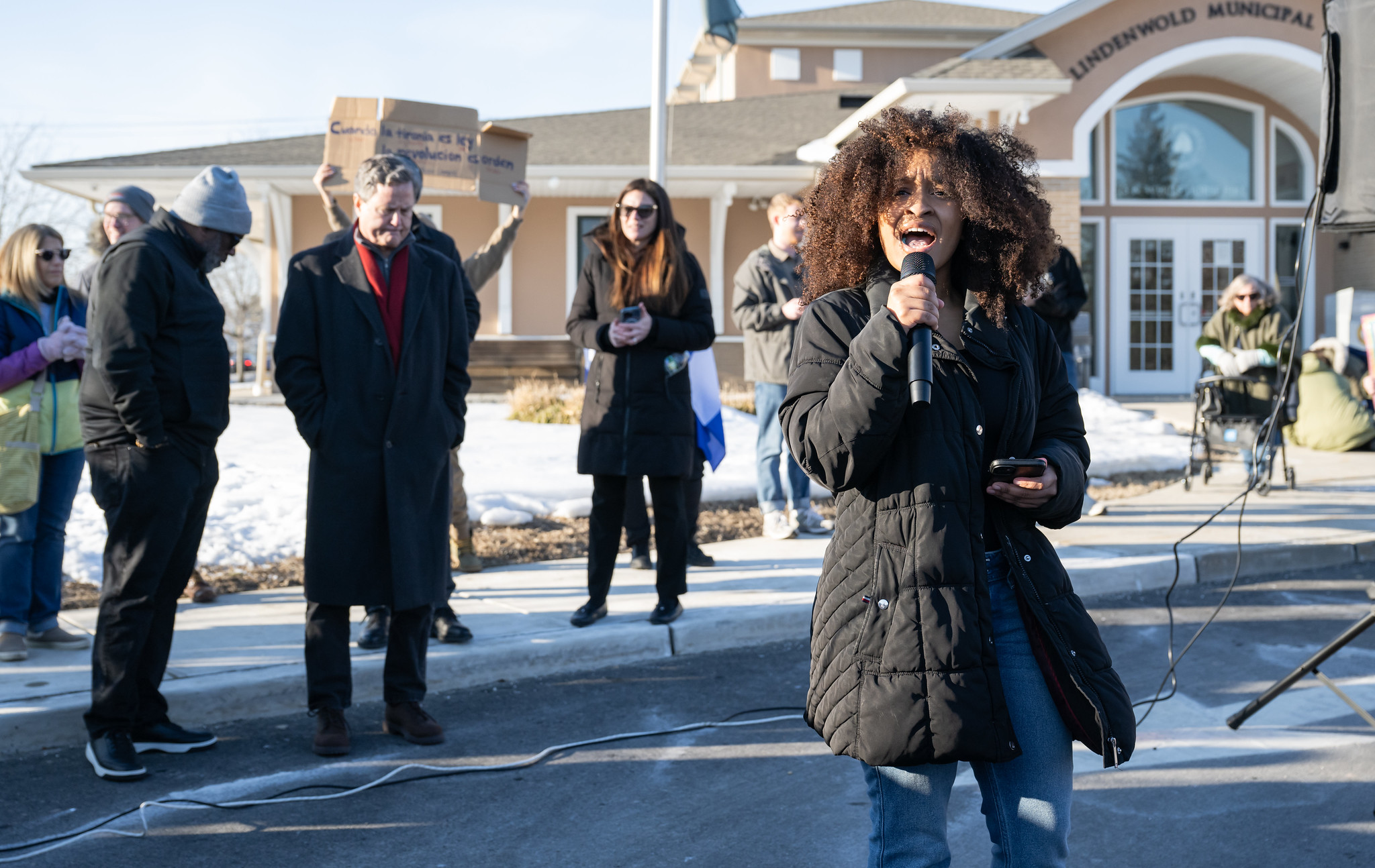I large group of people gather on the side of the road to protest the presence of ICE in Camden County. A street sign about the crowd reminds Laurel Spring to "Keep Left"