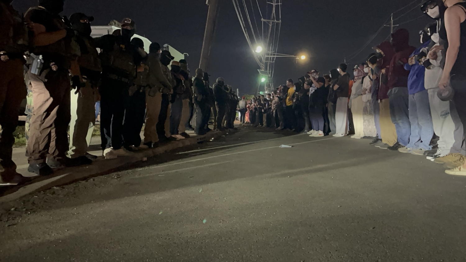A night picture taken from ground level. On the left is a line of police and on the right is a line of protestors